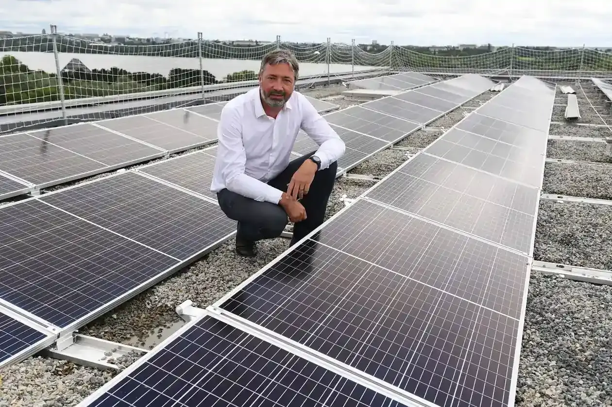 président directeur général de l'Ademe à genoux sur le toit du bâtiment à côté d'une rangée de panneaux solaires