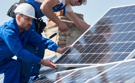 2 hommes installant un panneau solaire sur un toit, l'homme porte un casque de chantier blanc