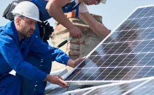 2 hommes installant un panneau solaire sur un toit, l'homme porte un casque de chantier blanc
