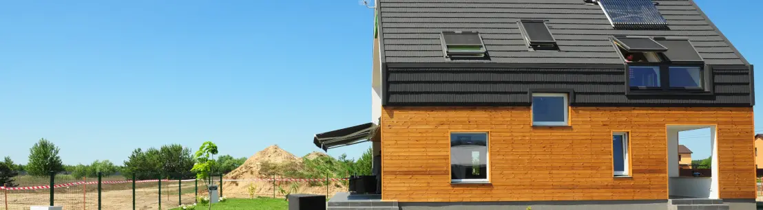 Une maison basse consommation en bois avec des panneaux solaires devant une pelouse verte