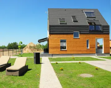 Une maison basse consommation en bois avec des panneaux solaires devant une pelouse verte
