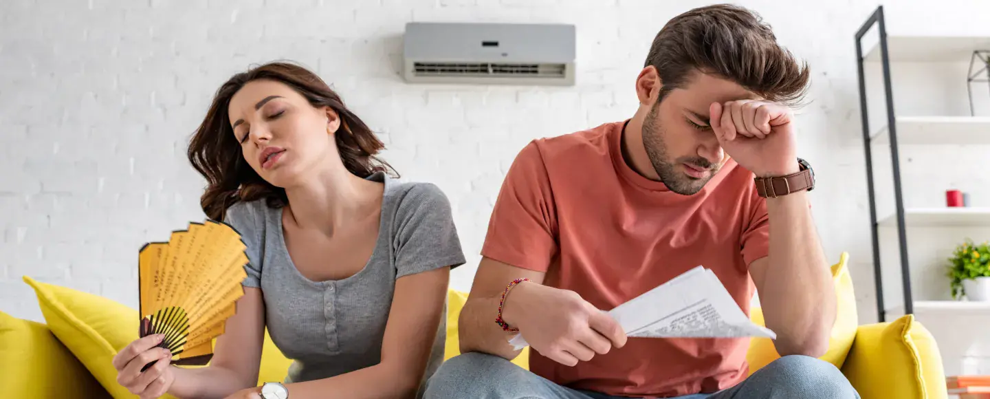 Un couple souffre de la chaleur et de la précarité énergétique en été dans leur logement sur un canapé jaune
