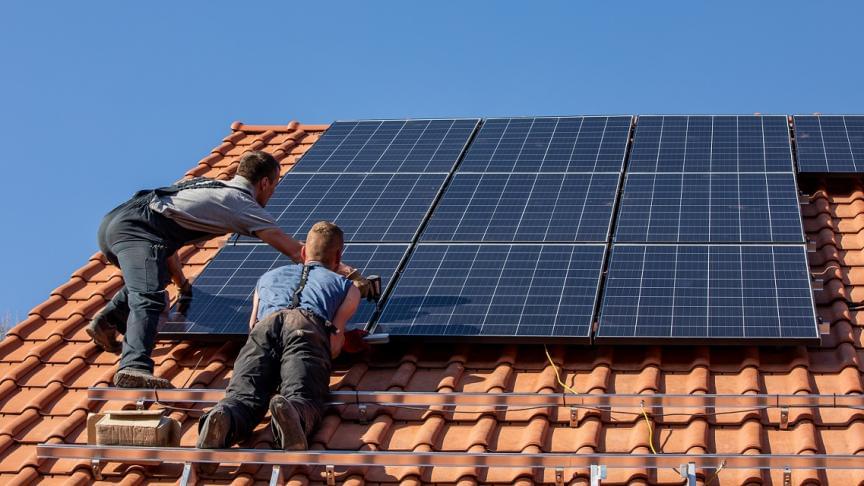 deux hommes en train de poser des panneaux solaires sur le toit d'une maison