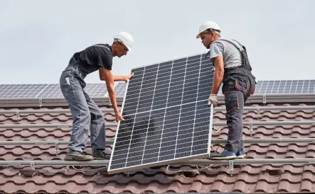 deux hommes portant un casque de chantier blanc qui installent un panneau solaire sur un toit marron