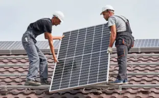 deux hommes portant un casque de chantier blanc qui installent un panneau solaire sur un toit marron