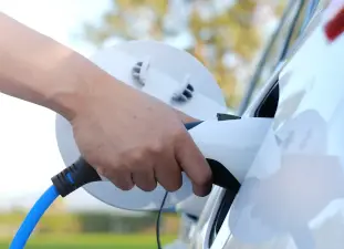 main qui recharge la batterie d'une voiture électrique blanche