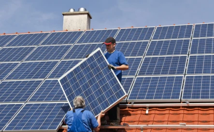 deux hommes qui posent un peanneau solaire sur un toit avec une cheminée